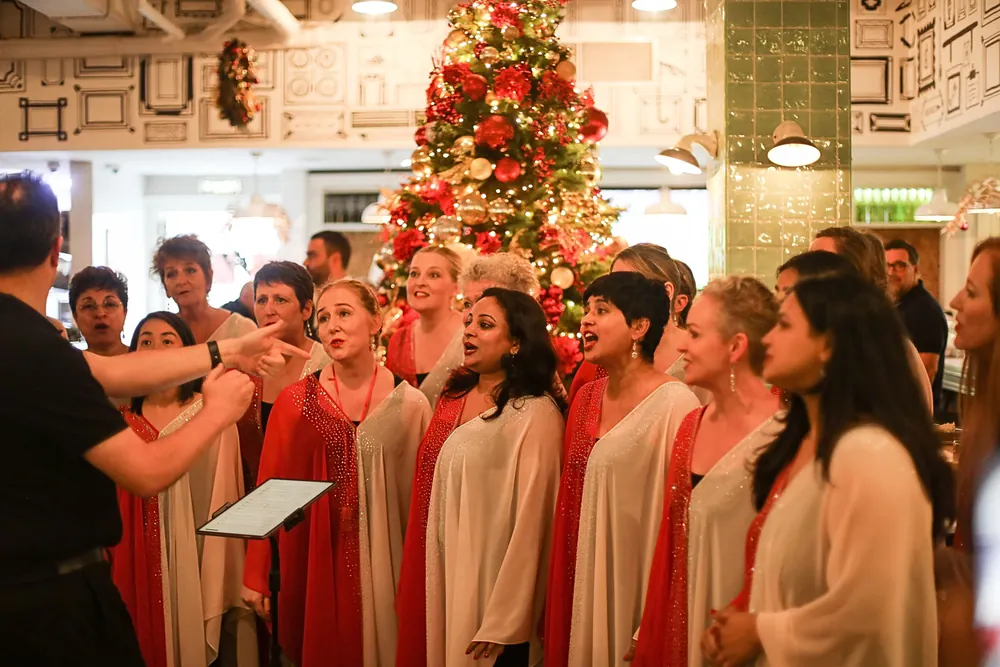A choir in red and cream robes singing in front of the Christmas tree at Maison Mathis