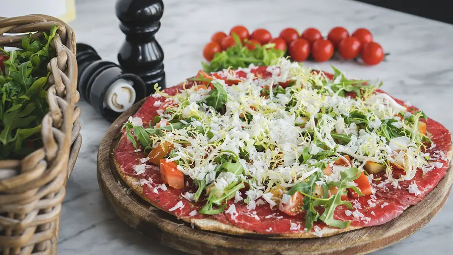 Beef carpaccio pizza topped with rocket, tomato and shaved cheese