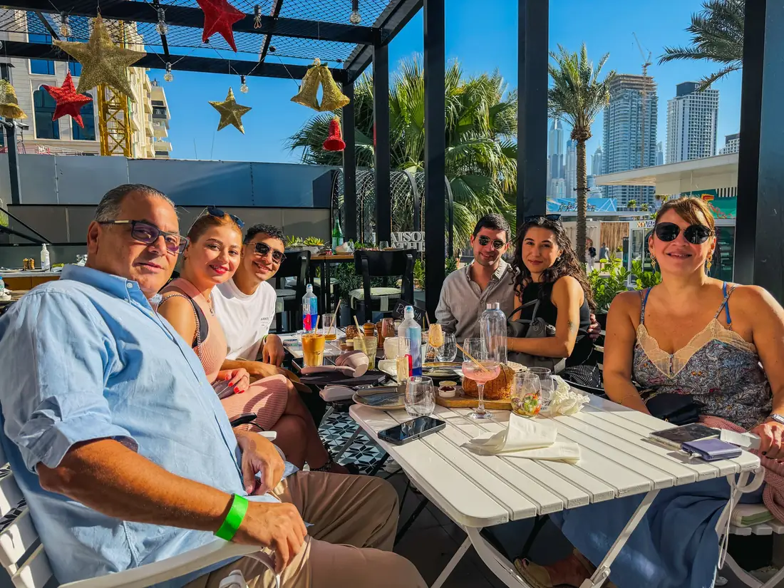 Guests at a sunny terrace table with palm trees and towers behind