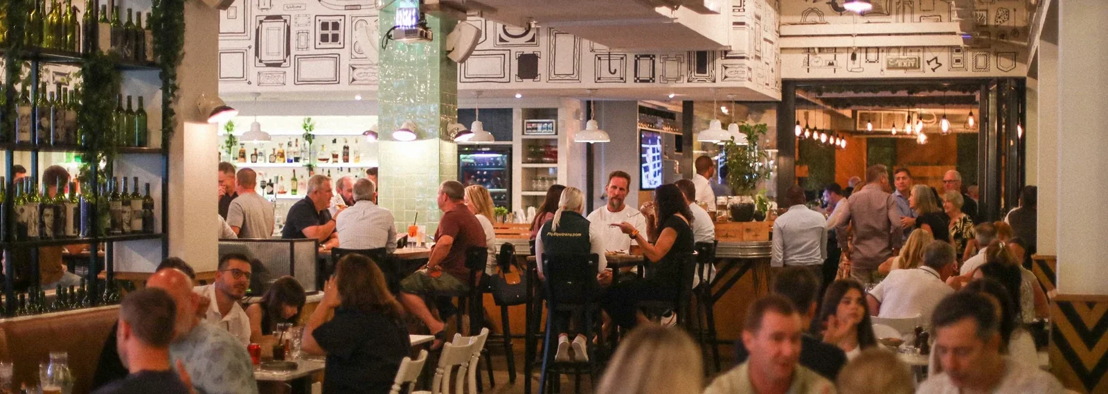 Guests at the bar and tables of a busy Maison Mathis dining room in the evening
