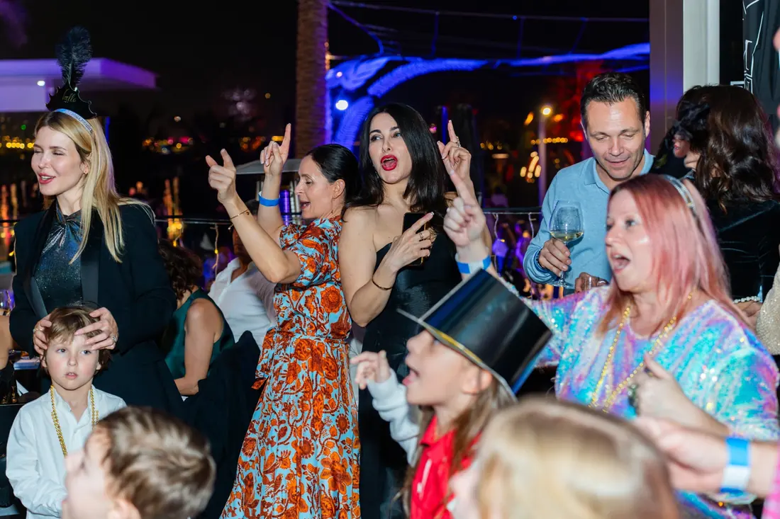 Guests celebrating New Year’s Eve with a child in a top hat, cheering and dancing
