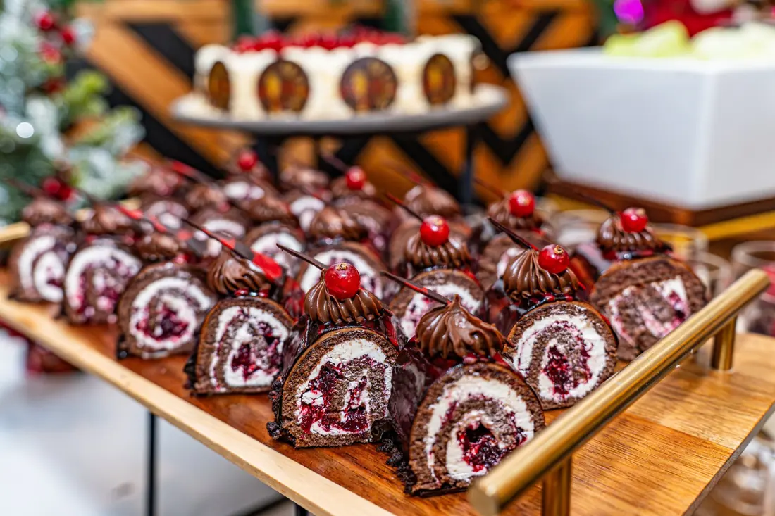 Mini chocolate Christmas logs topped with cherries on a wooden serving board