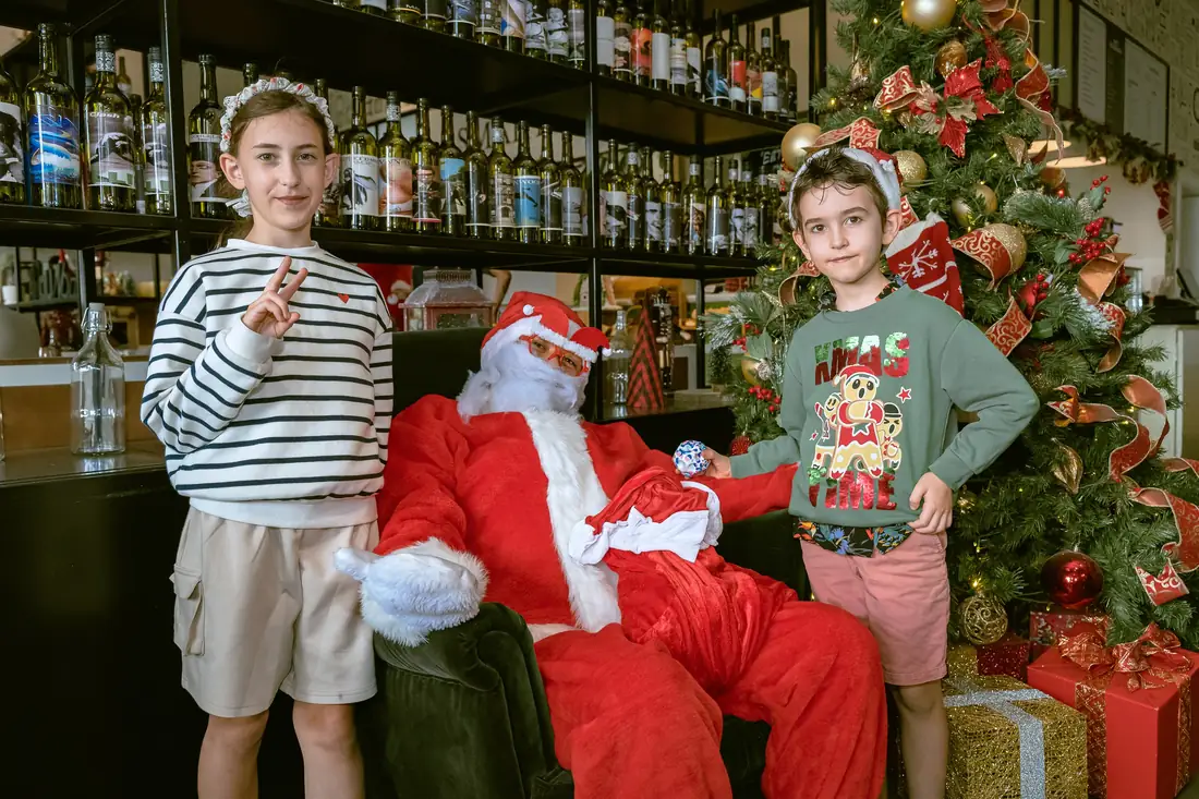 Two children posing with Santa in front of the bar and a Christmas tree