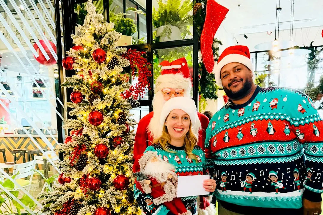 Two guests in Christmas jumpers with Santa beside a Christmas tree