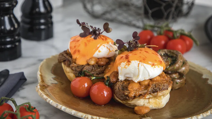 Two poached eggs with pulled beef and hollandaise on a rustic plate